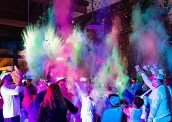 A crowd of people celebrating with colorful powder explosions in the air.