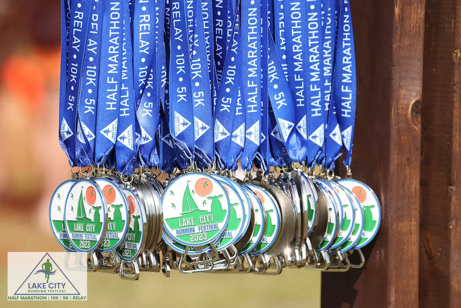 A row of shiny race medals with blue ribbons, featuring the Lake City Running Festival logo and the year 2023.