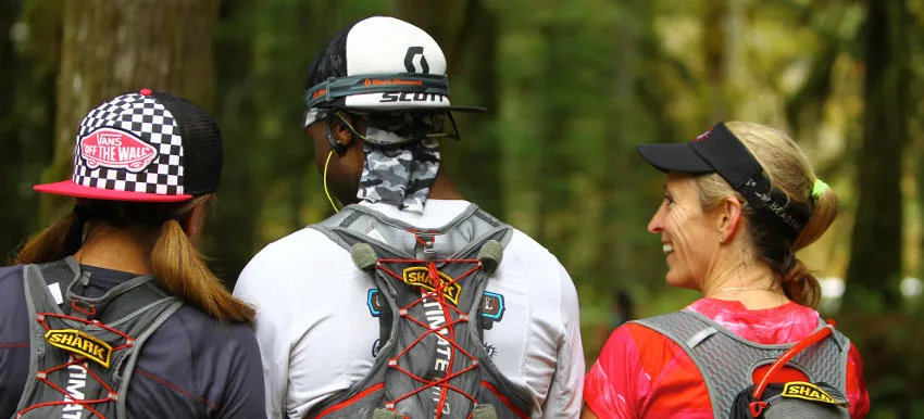 Three runners in a forest setting, two facing away and one looking to the side and smiling.