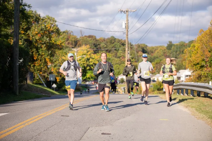 Runners on a road during a race, with trees and houses in the background.