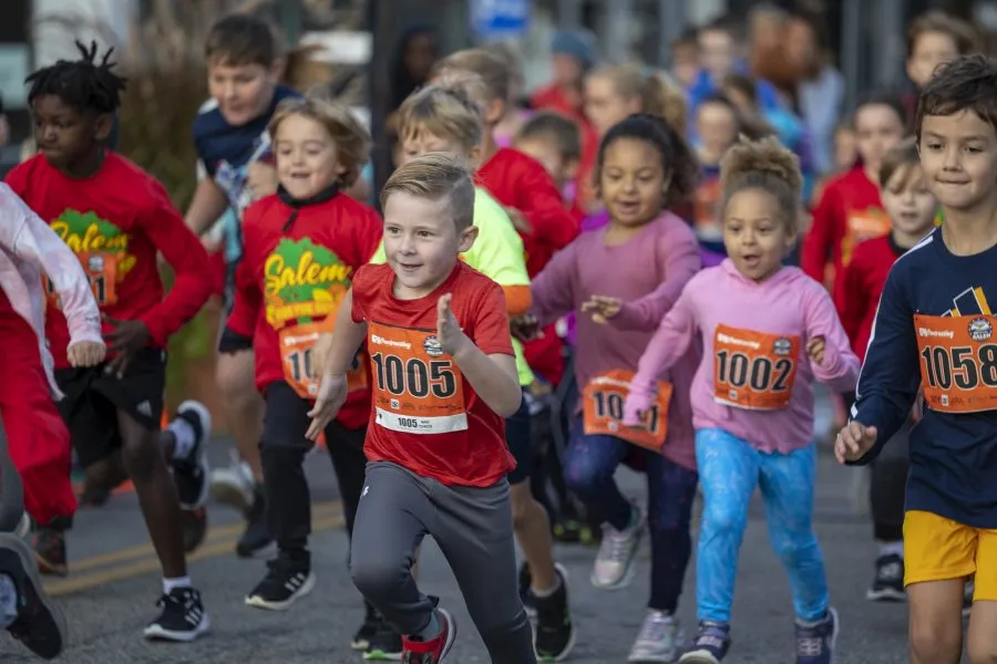 A group of young children running in a race, with bib numbers visible on their shirts.