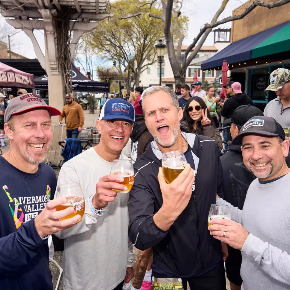 Four men smiling and holding glasses of beer, appearing to celebrate after a race.