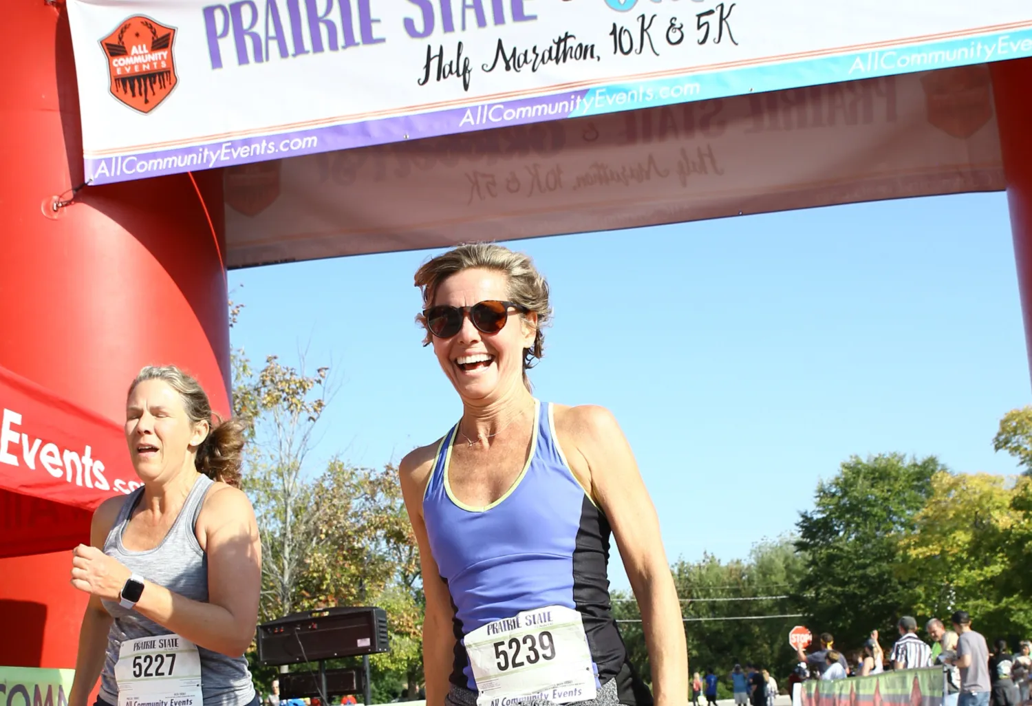 Two female runners smiling and laughing at the start line of the Prairie State Half Marathon, 10K & 5K.