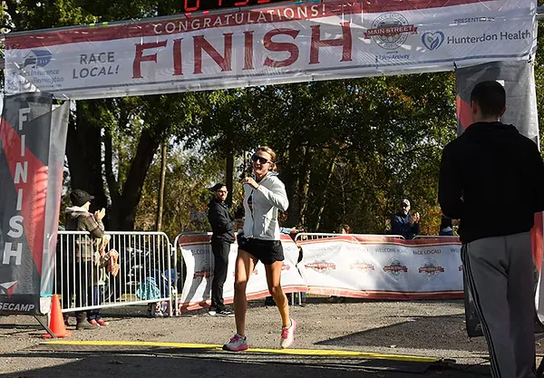 A female runner smiles as she crosses the finish line at a road race.