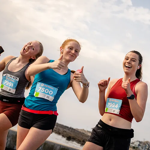 Three female runners smiling and giving thumbs up during a race.
