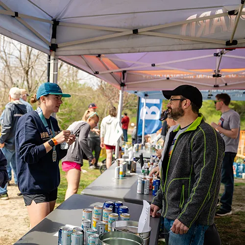 Runners gather at a refreshment tent after a race, with drinks and snacks on tables.