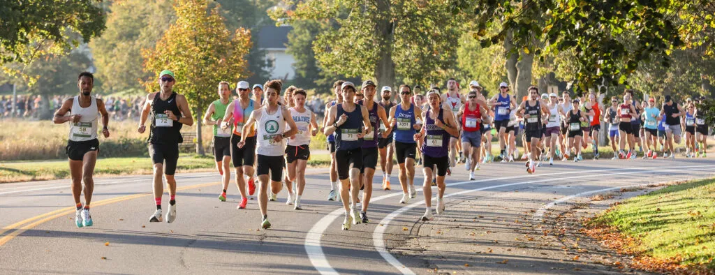 A group of runners participating in a road race, with trees and foliage lining the course.