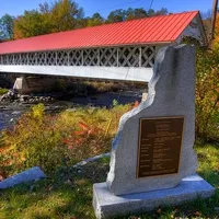 Covered bridge with a red roof and a stone monument in the foreground.