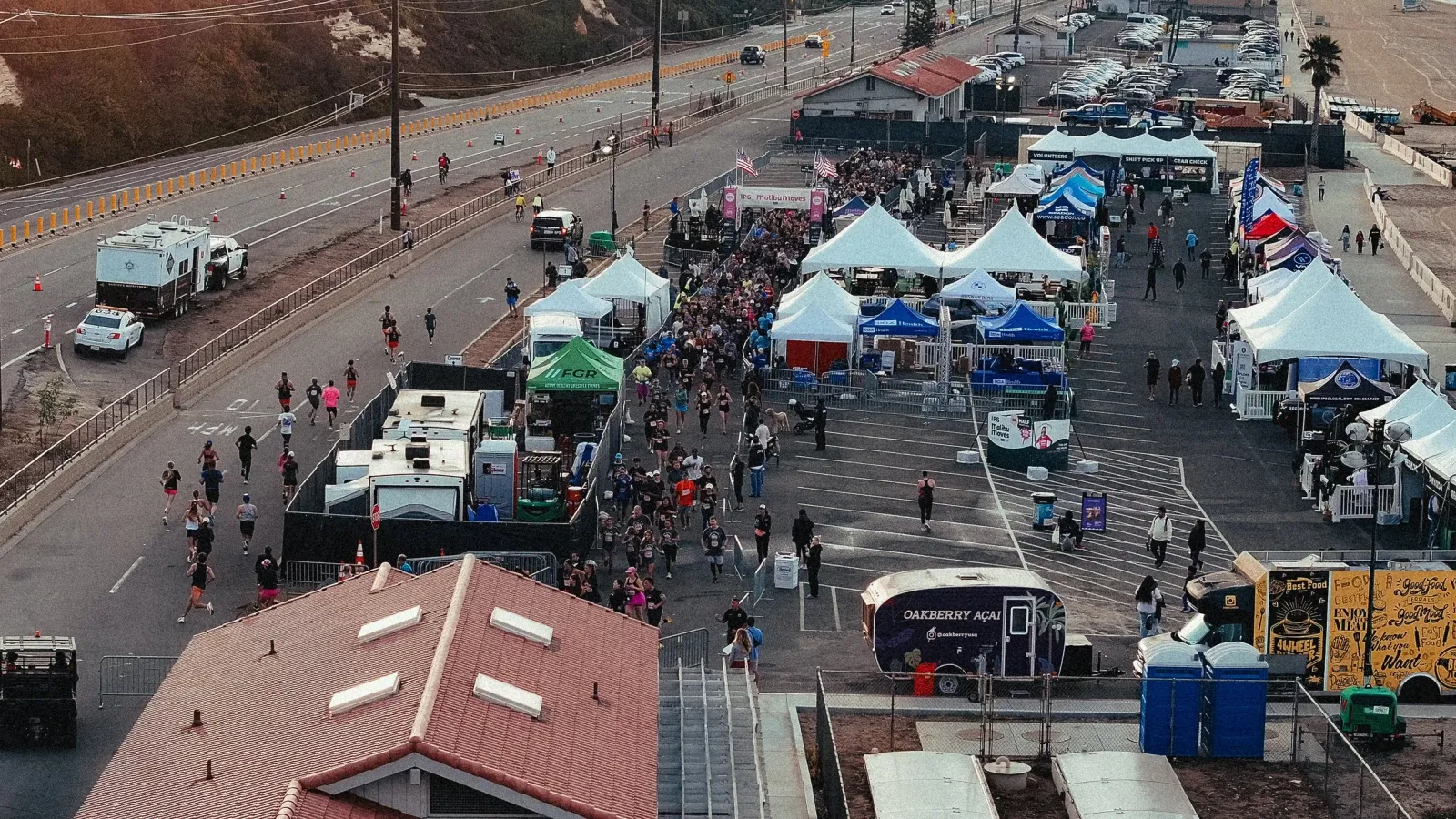 Overhead view of runners on a road course with tents and spectators in the background.