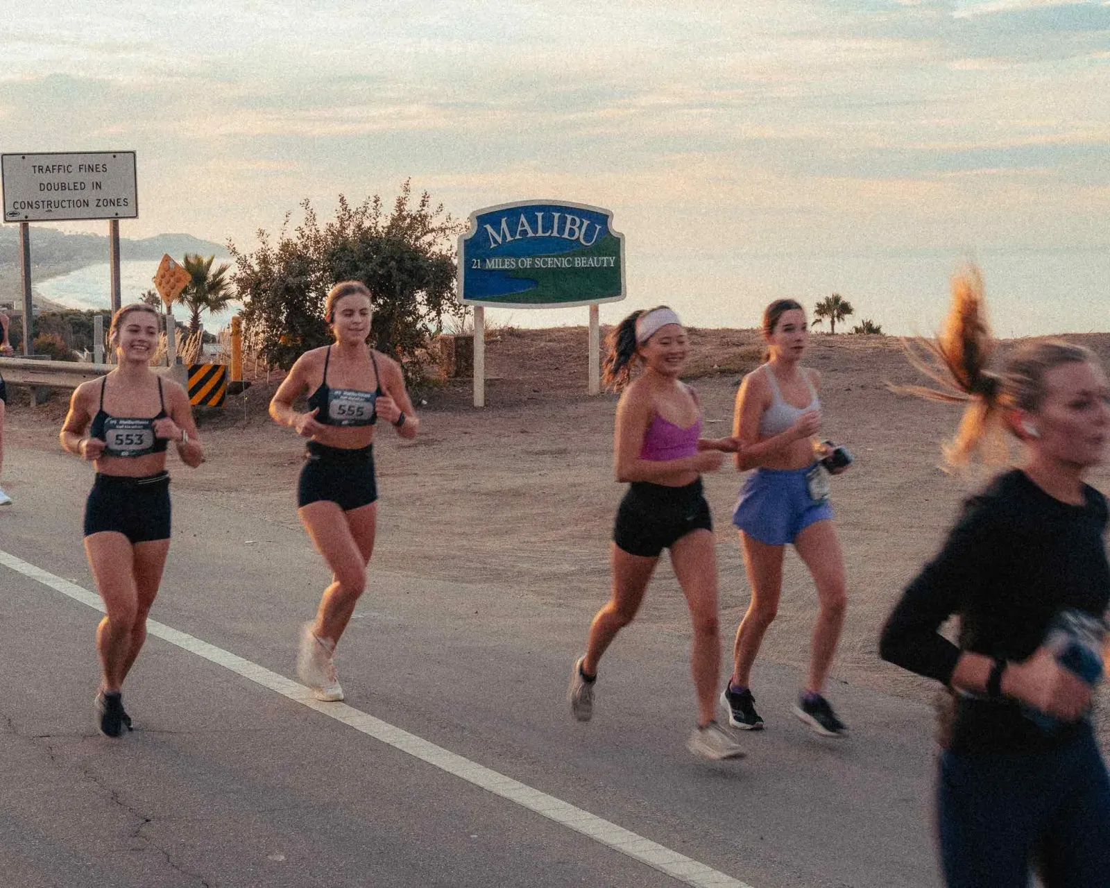 Runners on a road with the Malibu sign in the background at sunset.