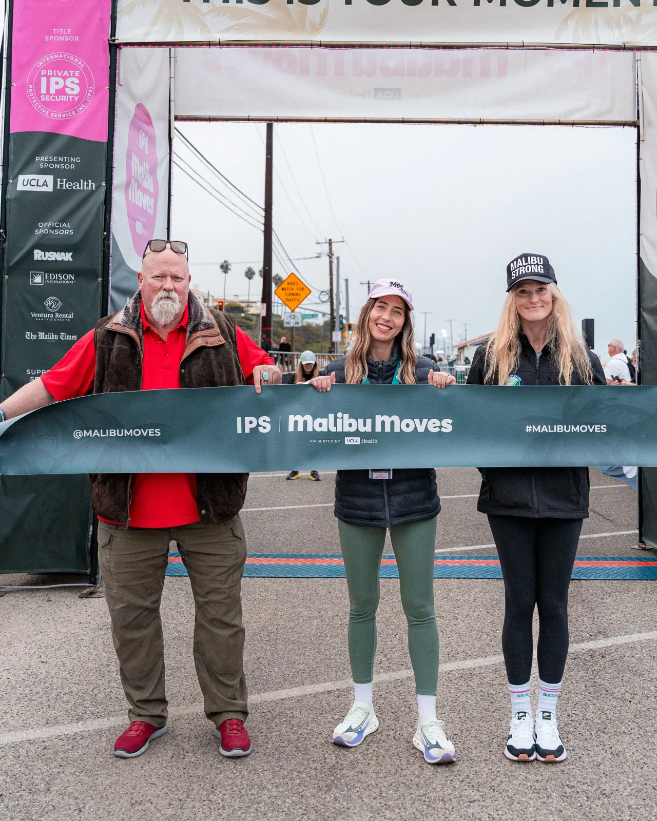 Three people smiling and holding a banner at the finish line of the Malibu Moves race.