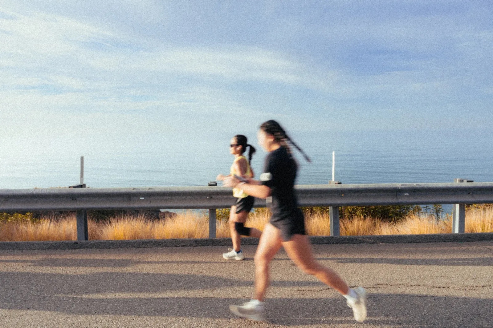 Two runners on a road with the ocean in the background.