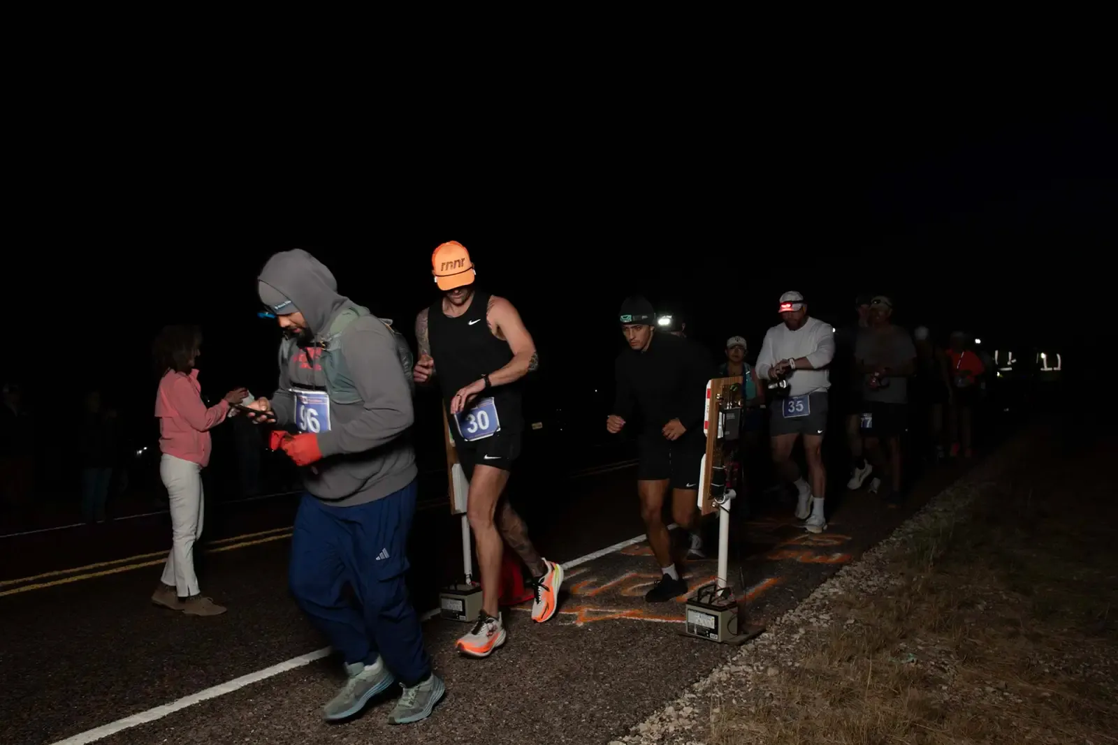 Runners starting a race at night, with bib numbers visible.