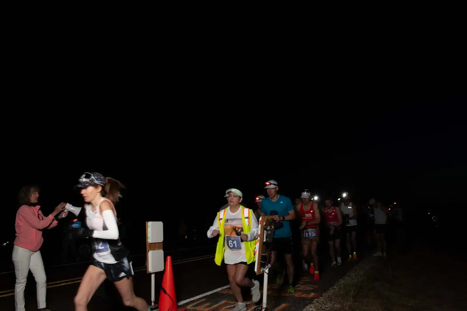 Runners starting a race at night, with a volunteer offering water.