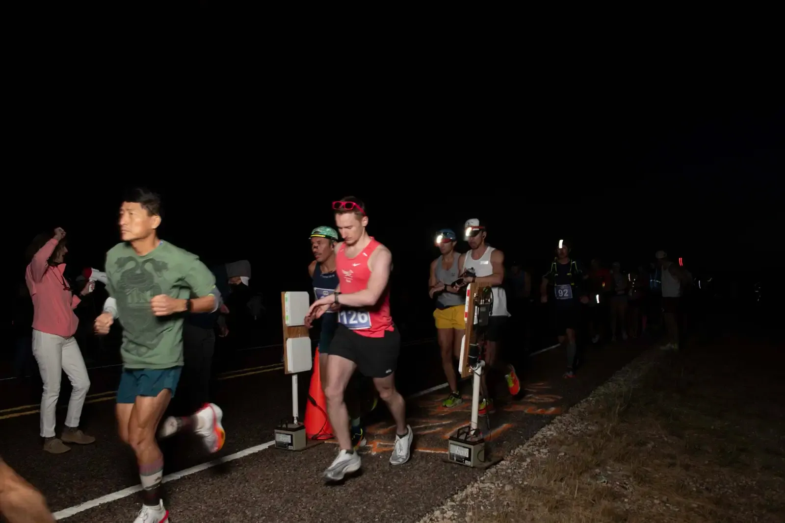 Runners starting a race at night, with headlamps on and bib numbers visible.