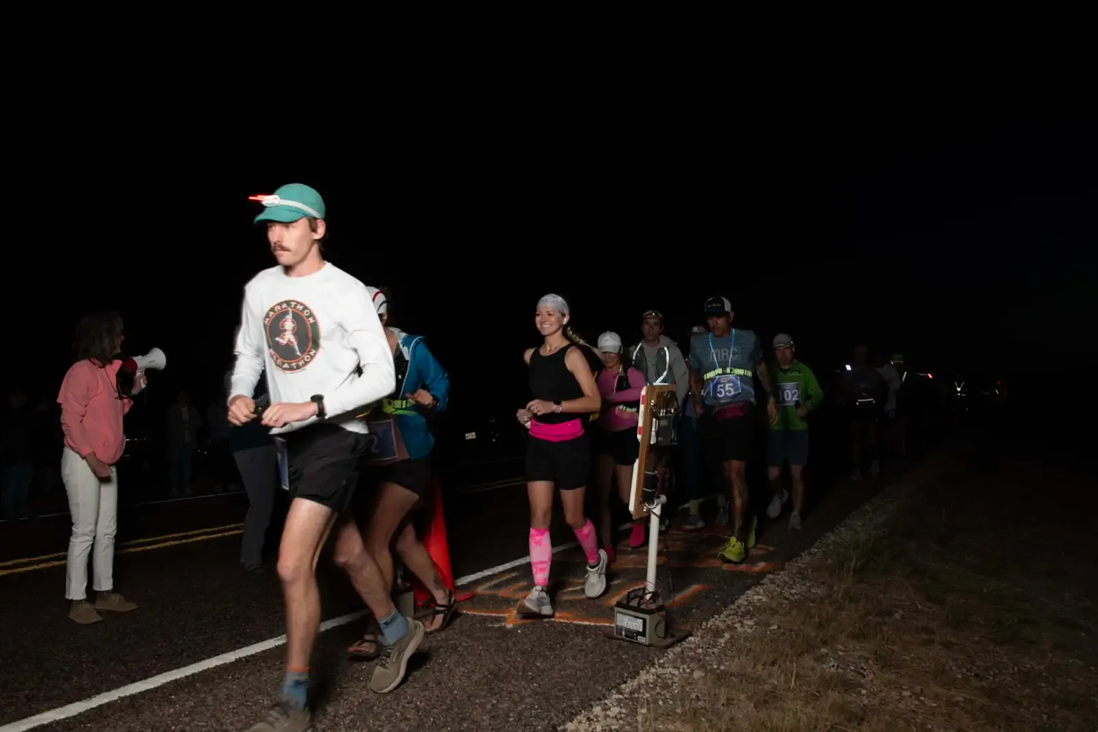 Runners starting a race at night, with some wearing headlamps.