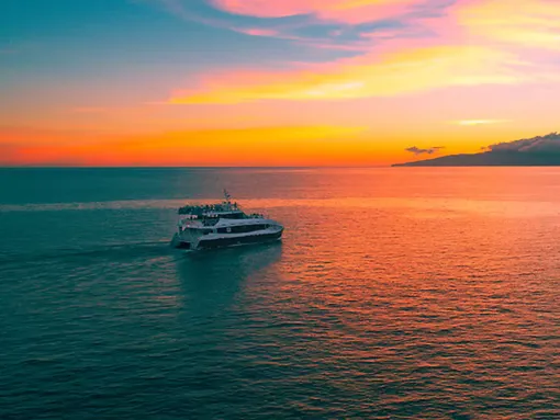 A boat sails on the ocean during a vibrant sunset with orange and pink hues in the sky.