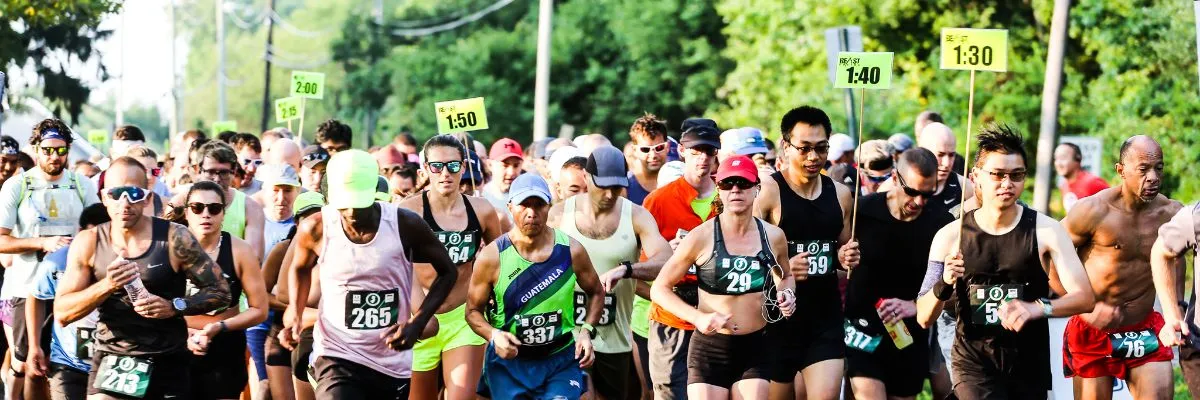 A large group of runners are starting a race, with some holding signs indicating pace times.