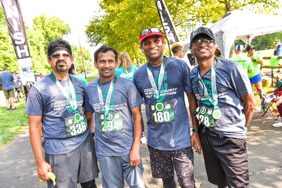 Four smiling runners wearing race t-shirts and medals pose for a photo near a finish line banner.