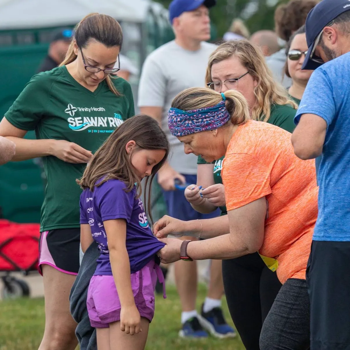 A woman helps a young girl adjust her race bib before the start of the Mercy Health Seaway Run.