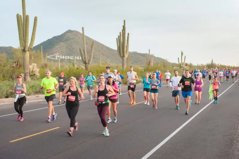 A group of runners participating in the Mesa Marathon, with the Phoenix sign and saguaro cacti visible in the background.