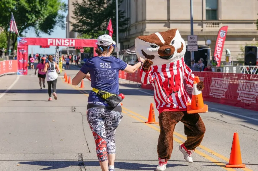 A runner gives a high-five to a mascot near the finish line of a race.