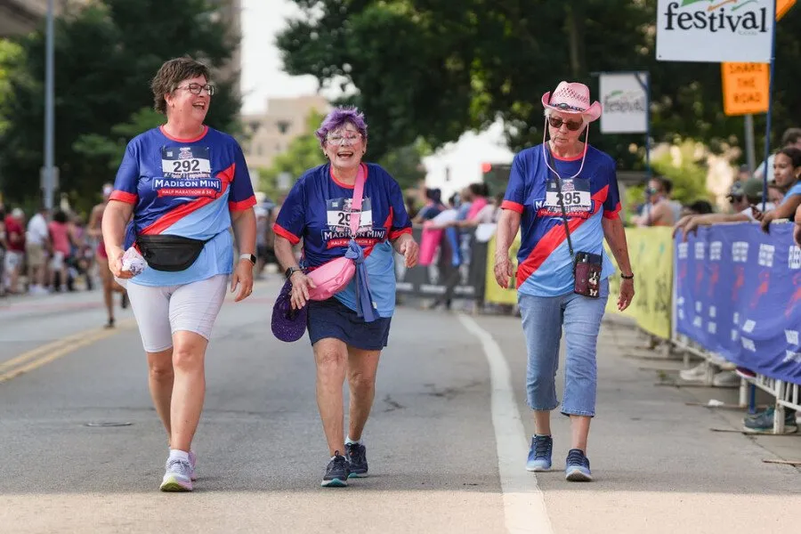 Three women in matching race t-shirts walking on a road during a half marathon event, smiling and enjoying the experience.