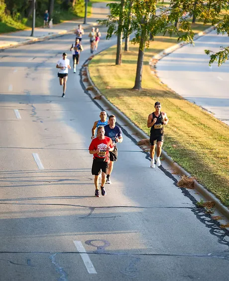 Runners on a paved road with trees and grass on the side.