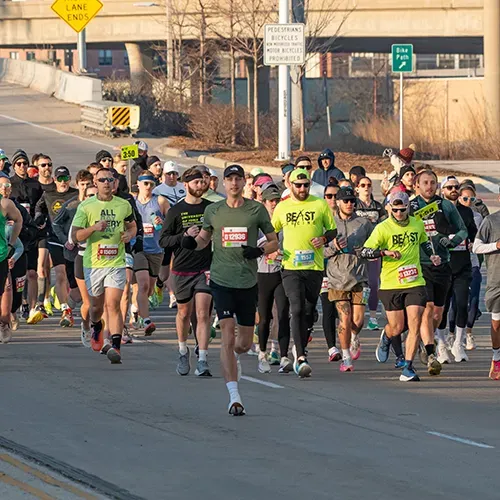A group of runners on a road during a race, with some wearing bright green shirts and others in darker colors.