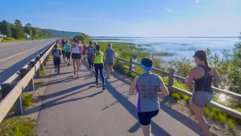 A group of runners on a paved path next to a road and a body of water.
