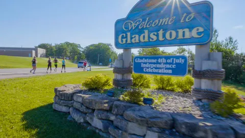 Runners on a road passing a welcome sign for Gladstone.