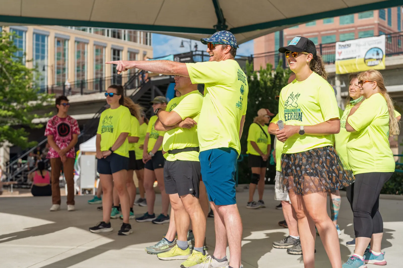 A group of runners in bright yellow shirts stand together, with one man pointing forward.