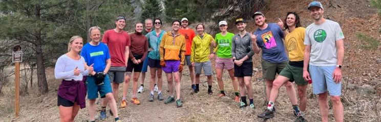 A group of runners smile and pose for a photo on a dirt trail surrounded by trees.