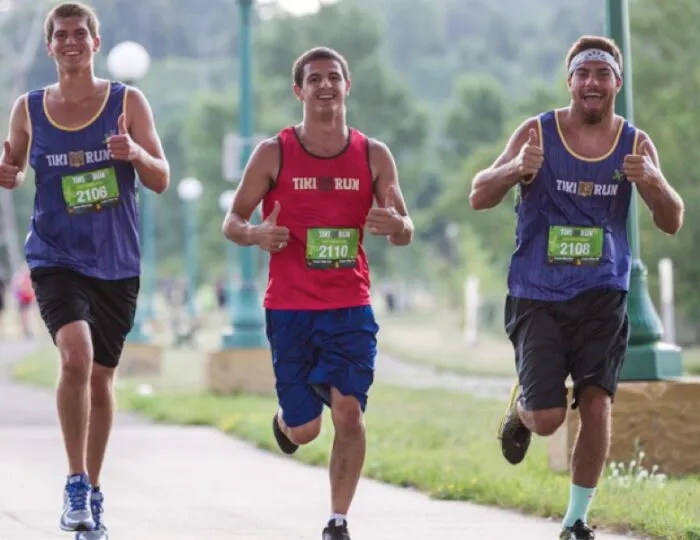 Three young men running a race, all giving thumbs up.