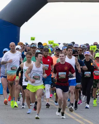 Runners starting a race under a blue archway, with many participants in the foreground and background.
