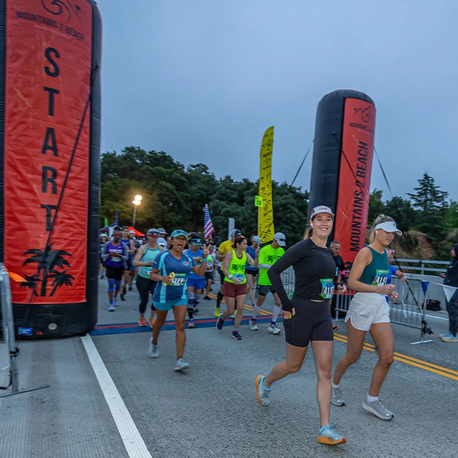 Runners starting the Mountains 2 Beach Marathon and Half, passing under an inflatable start arch.