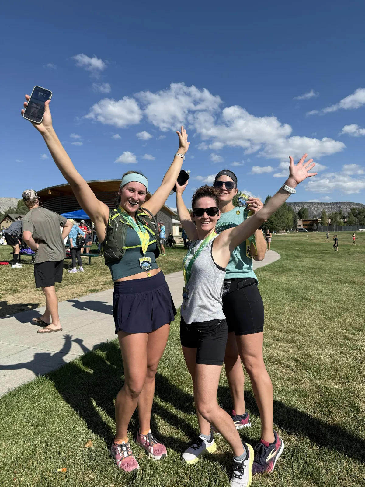 Three women with medals around their necks and arms raised in celebration, smiling at the camera.