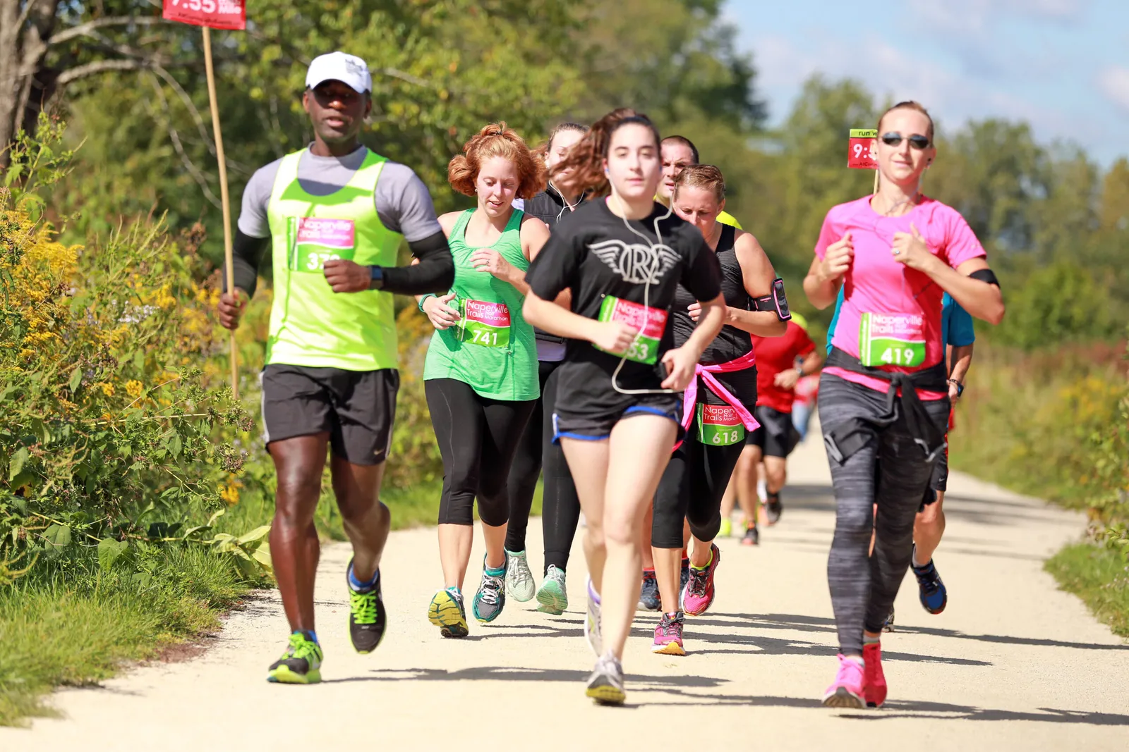 A group of runners on a trail, with a mile marker sign in the background.