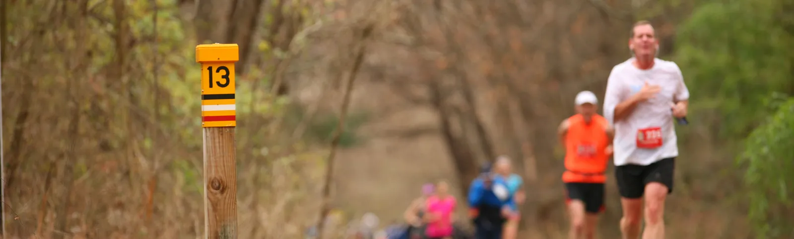 Runners on a wooded path with a mile marker indicating mile 13.
