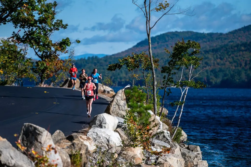 Runners on a road next to a lake with mountains in the background.