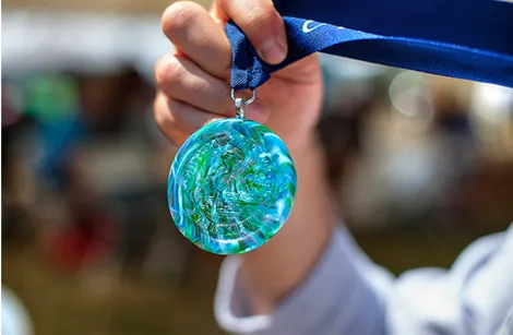 A hand holds up a colorful race medal with a blue ribbon.