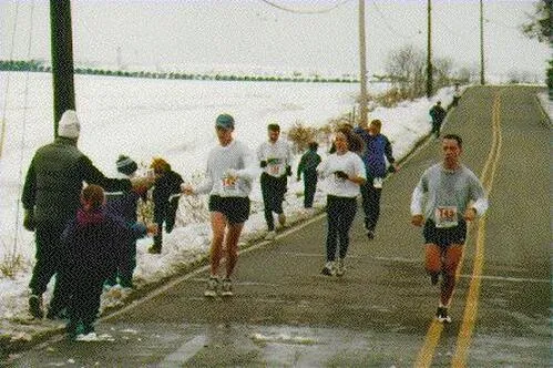 Runners participating in a half marathon on a snowy road, with spectators on the side.