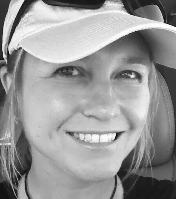 Close-up black and white photo of a smiling woman wearing a white baseball cap and sunglasses.
