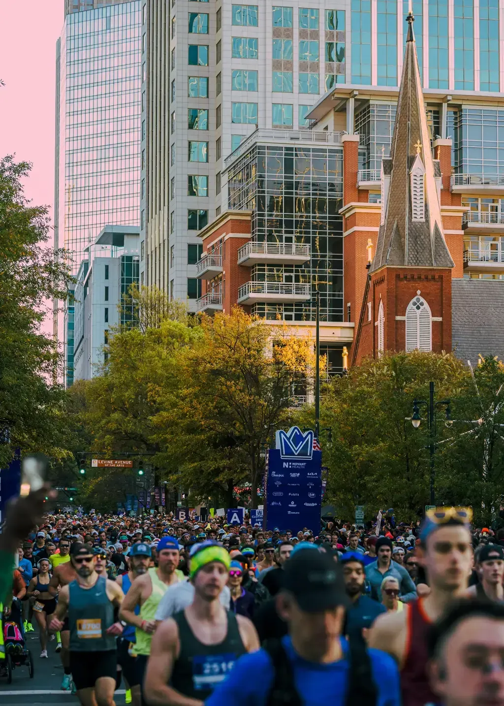 A large group of runners participating in a marathon on a city street, with tall buildings and trees in the background.