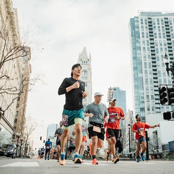 Runners in a race on a city street with tall buildings in the background.