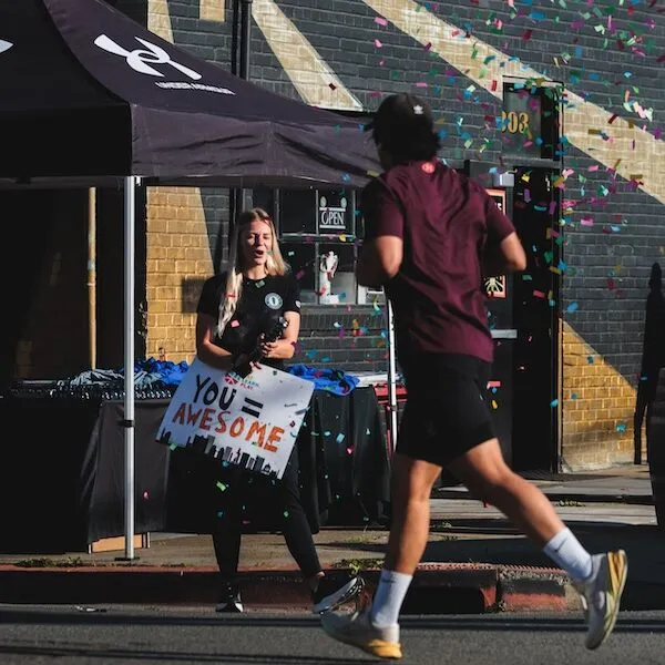 A runner passes by a person holding a sign that says 'YOU = AWESOME' as confetti falls.