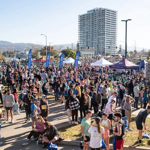 A large crowd of runners gathered before a race, with tents and a tall building in the background.