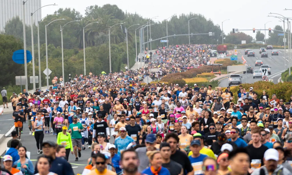 A large crowd of runners participating in a race on an urban road.
