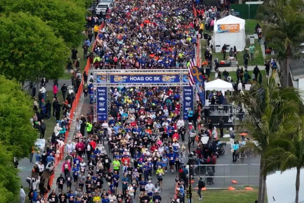 A large crowd of runners starting the HOAG OC 5K race under an archway.