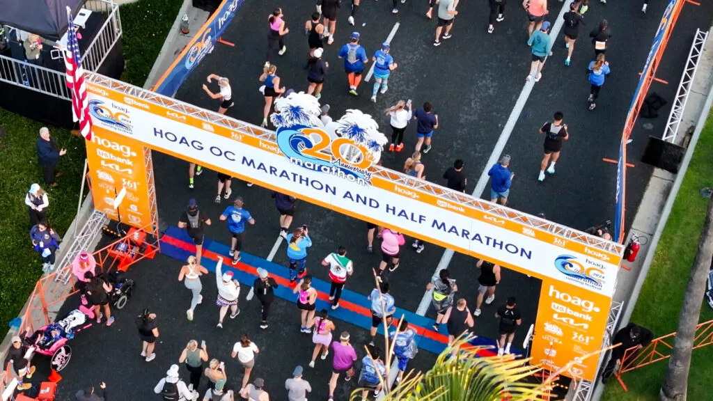 Runners crossing the finish line of the Hoag OC Marathon and Half Marathon under a large orange archway.